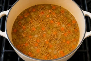 Chicken broth, vegetables, herbs, and grains simmering in a soup pot for Mendocino Farms lemon chicken soup recipe